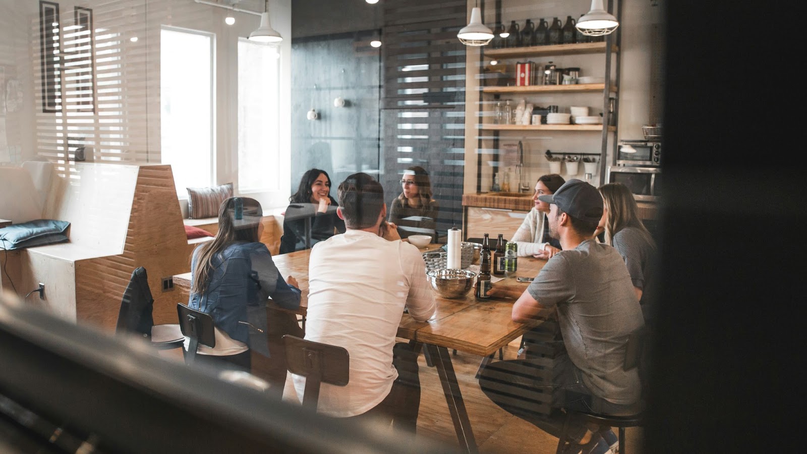 A imagem mostra um grupo de pessoas sentadas ao redor de uma mesa de jantar, engajadas em uma conversa. Há pelo menos sete pessoas visíveis na cena, algumas sentadas em cadeiras e outras em pé. A mesa é cercada por vários itens, incluindo várias garrafas, copos e uma tigela.

Além das pessoas e dos utensílios de mesa, há dois sofás na sala, um localizado perto do lado esquerdo da imagem e outro no lado direito. Um micro-ondas pode ser visto ao fundo, sugerindo que o encontro pode estar ocorrendo em uma cozinha ou área de jantar.