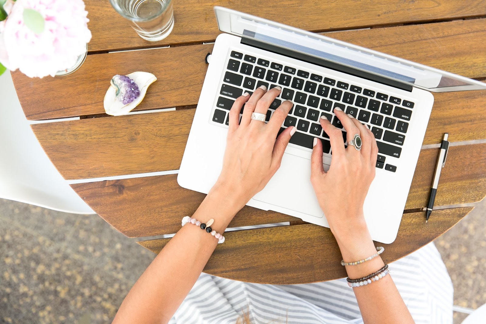 Nesta imagem, podemos ver uma pessoa sentada em uma mesa de jantar, trabalhando em um laptop. As mãos da pessoa estão no teclado, digitando ou navegando na internet. O laptop ocupa uma parte significativa da superfície da mesa.

Além do laptop, há alguns outros itens na mesa. Uma xícara pode ser vista perto do canto superior esquerdo, enquanto um celular está localizado no lado direito da mesa. Uma garrafa também está presente, posicionada no canto superior esquerdo da mesa.