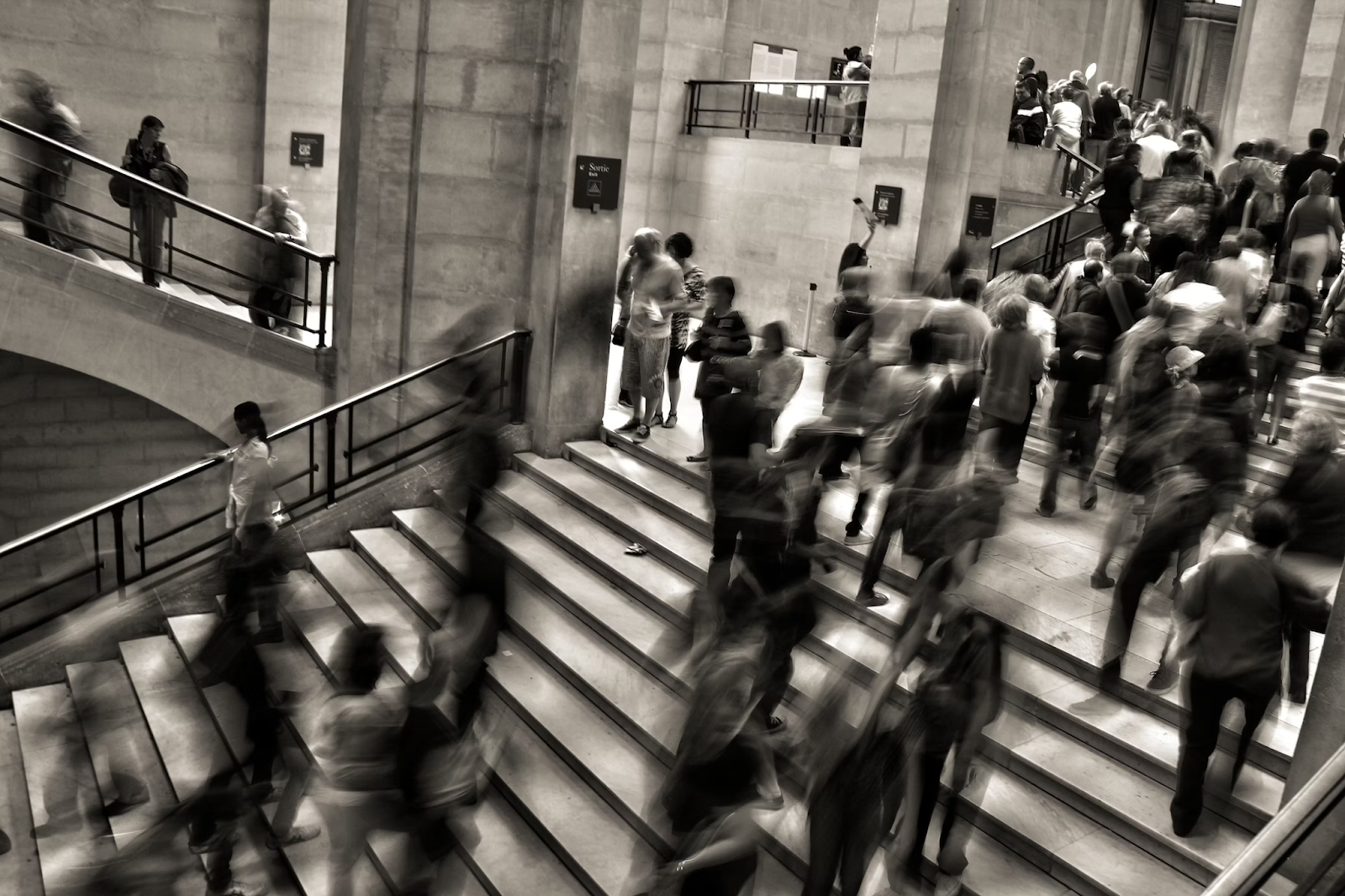 foto em preto e branco, demonstrando pessoas subindo e descendo escadas em um prédio.